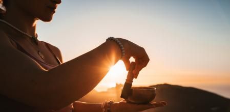 Beautiful girl doing meditation using a Tibetan singing bowl during the sunrise in a mountainous landscape and seascape in Majorca. Color editing with slightly grain. Part of a series.