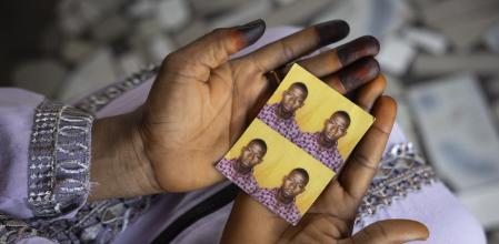 Mariama Sylla, sister of Ousmane Sylla, holds photos of him in their house at Matoto Bonagui, a suburb of Conakry, Guinea, Monday, April 8, 2024. Sylla had landed on Italian shores a year before his death in Feb. 4, 2024, one of tens of thousands of people who pay migrant smugglers hundreds or thousands of euros to cross the Mediterranean to reach Europe. He had no visa, and had been ordered to leave after admitting that he had lied about being a minor. (AP Photo/Misper Apawu)