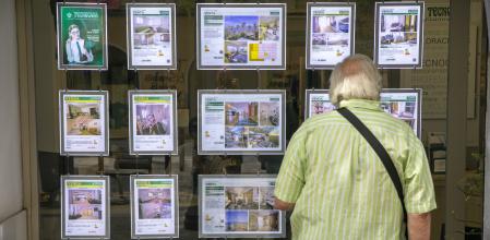 UN HOMBRE MIRA CARTELES DE VENTA Y ALQUILER DE PISOS EN UNA INMOBILIARIA DE LA BARCELONETA