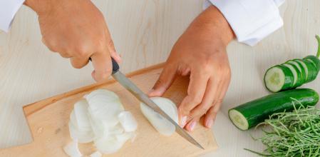 manos de un hombre cortante cebolla sobre una mesa de cocina de madera