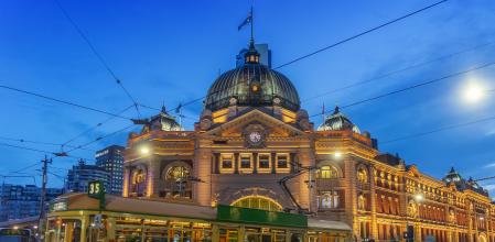 A tram passes Flinders Street Station at dusk.