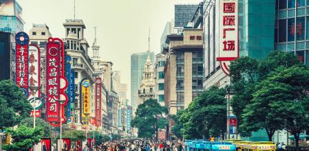 Crowds walk below neon signs on Nanjing Road. The street is the main shopping district of the city and one of the world's busiest shopping districts.