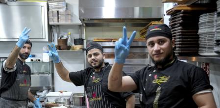 Syrian refugees who immigrated to Germany due to the war condition in Syria, flash the victory sign to support free Syria while working in a Syrian restaurant in Berlin, Tuesday, Dec. 10, 2024. (AP Photo/Ebrahim Noroozi)