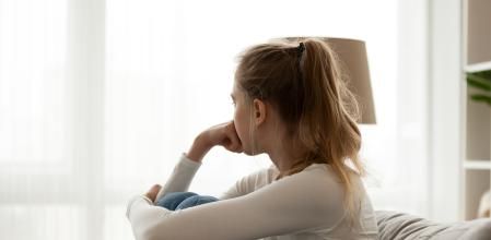 Side view young woman looking away at window sitting on couch at home. Frustrated confused female feels unhappy problem in personal life quarrel break up with boyfriend or unexpected pregnancy concept