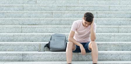 Sad and frustrated hispanic teenager sitting on stairs and holding his head. Anxiety and depression in adolescence concept.