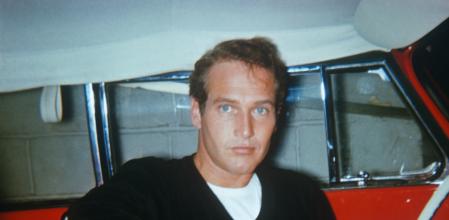 Paul Newman in the 1950's, sitting in a red car with white interior. The photograph was taken with a star flash camera. The photographer was walking with his family and saw this unknown actor he recognized--after 