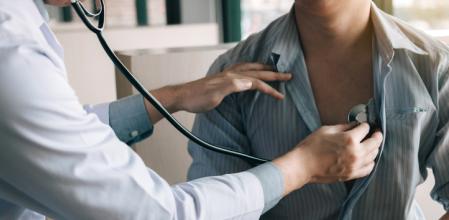 Un doctor está usando un estetoscopio para escuchar los latidos del corazón del paciente anciano.