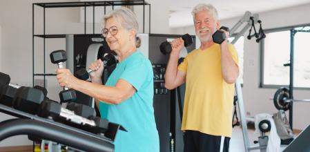 Pareja de ancianos en ropa deportiva haciendo ejercicio con mancuernas en el gimnasio