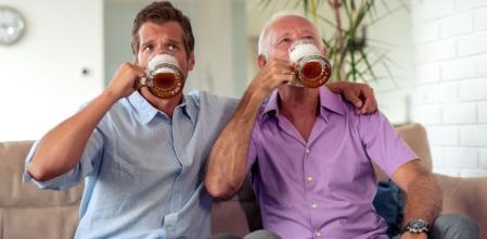 Padre e hijo beben tranquilamente una cerveza mientras ven la TV