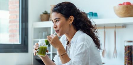 Mujer bebiendo un zumo detox de frutas en la cocina de casa.
