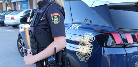 Imagen de una agente y de un coche patrulla de la Policía Nacional.