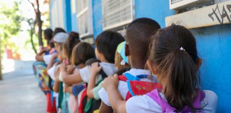 Varios niños hacen fila con sus mochilas, antes de entrar al Centro Chapotea con la Asociación Barró en Vallecas, a 20 de julio de 2022, en Madrid (España). Este centro pertenece al programa CaixaProinfancia que facilita que 35 entidades de la Comunidad de Madrid promuevan este verano colonias urbanas, centros abiertos y campamentos para más de 4.250 niños y adolescentes en situación de vulnerabilidad, riesgo de pobreza o exclusión.