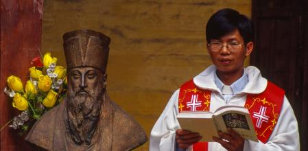 Un sacerdot de l’Esglésiacatòlica xinesa llegeix l’Evangelial costat d’un bust del jesuïta Matteo Ricci