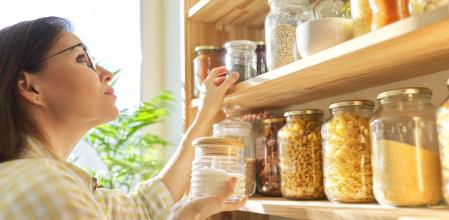 Una mujer buscando comida en su despensa ordenada con botes y tarros