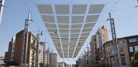 Unas personas transitan a la sombra de un umbráculo en la Rambla de Sants en Barcelona este domingo 