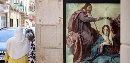 Una dona amb vel passa vora el cartell d'una representació catòlica a Jumella&nbsp;