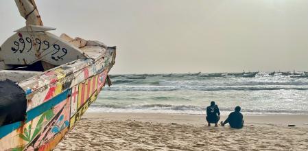 Un par de inmigrantes delante de un cayuco, como los que suelen llegar a Canarias, en la costa mauritana