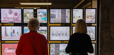 Una pareja mirando el escaparate de una inmobiliaria con las ofertas de pisos y casas de alquiler y venta 