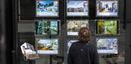 UNA MUJER OBSERVA EL ESCAPARATE DE UNA INMOBILIARIA CON LA OFERTA DE VIVENDAS EN LA CIUDAD DE BARCELONA