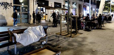 Una persona duerme en un banco en los alrededores del mercado de Sant Antoni 