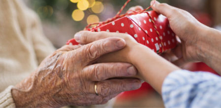 Manos de una persona mayor recibiendo un regalo de Navidad envuelto en papel rojo.