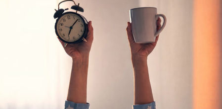 Persona levantando un despertador y una taza de café al despertar por la mañana