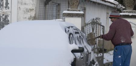Un hombre retira con una pala la nieve acumulada sobre su coche en la localidad cántabra de Bolmir este martes. Varias carteras autonómicas están afectadas por la nieve y precisan cadenas para circular