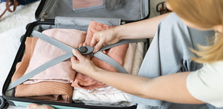 Persona cerrando una maleta con ropa doblada y correas de sujeción para optimizar el espacio.