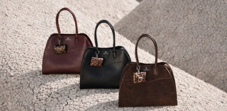 Tres bolsos de piel de silueta East-West en tonos burdeos, negro y marrón, colocados sobre una superficie rocosa clara, con diseño estructurado y detalle animal print