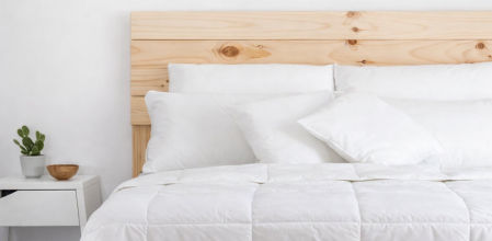 Cama vestida con edredón nórdico blanco y almohadas a juego sobre cabecero de madera clara