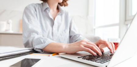 Persona trabajando con un portátil sobre una mesa en un entorno doméstico, ideal para estudio o teletrabajo.