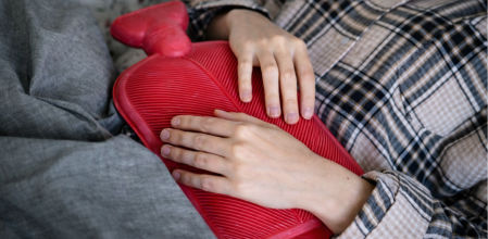 Persona recostada sosteniendo una bolsa de agua caliente roja sobre el abdomen para alivio del dolor