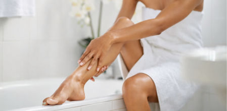 Mujer sentada tocándose la pierna suave recién depilada en un baño luminoso