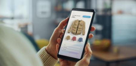 Una mujer usando su teléfono inteligente en una tienda de ropa en línea para elegir y comprar una chaqueta