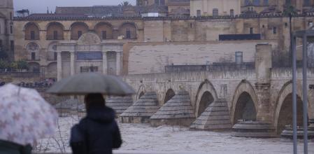 Dos personas observan ayer el puente romano de Córdoba, con la mezquita-catedral al fondo, y el Guadalquivir al límite de su capacidad