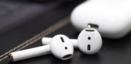 Auriculares inalámbricos tipo AirPods en color blanco junto a su estuche de carga sobre una superficie oscura