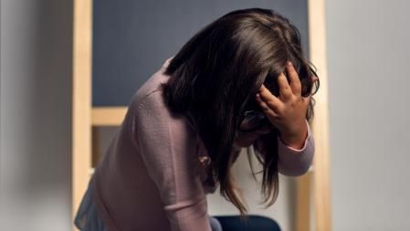 portrait of displeased and angry little girl holding hand on face and having negative expression.blackboard in background.
