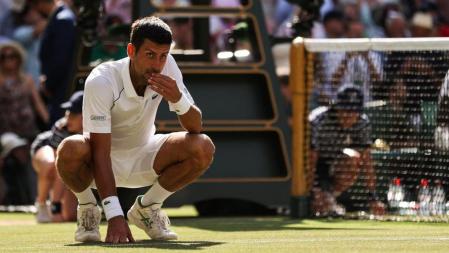 TOPSHOT - Serbia's Novak Djokovic reacts eating the grass from the court to beating Australia's Nick Kyrgios during their men's singles final tennis match on the fourteenth day of the 2022 Wimbledon Championships at The All England Tennis Club in Wimbledon, southwest London, on July 10, 2022. (Photo by Adrian DENNIS / AFP) / RESTRICTED TO EDITORIAL USE