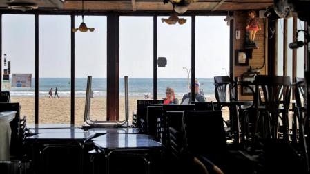 GRAFCVA2978. VALENCIA, 14/03/2020.- Dos personas observan el interior de un restaurante de la playa de La Malvarrosa de Valencia que permanece cerrado tras la publicación del decreto de la Generalitat de cerrar todos los bares y restaurantes de la Comunitat Valenciana. EFE/Manuel Bruque