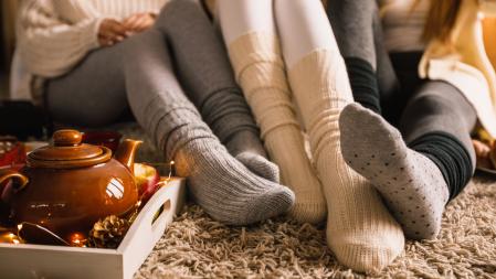 Lower section of three unrecognizable young girlfriends sitting on the bedroom floor in their cozy socks and hanging out together while enjoying some warm tea on a cold autumn day.
