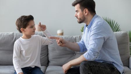 Angry strict father scolding lecturing naughty stubborn little son, unhappy annoyed dad quarreling, talking with preschool child boy, sitting on couch together, family conflict concept (Angry strict father scolding lecturing naughty stubborn little so