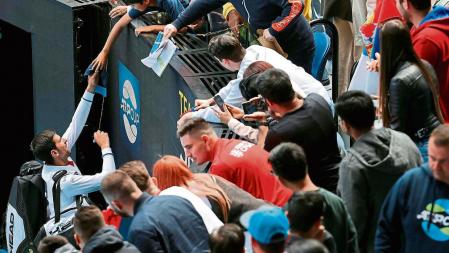 Serbia's Novak Djokovic (L) gives autographs to his fans at the end of group A men's doubles tennis match against Canada's Milos Raonic and Denis Shapovalov on day one of the 2021 ATP Cup in Melbourne on February 2, 2021. (Photo by DAVID GRAY / AFP) / -- IMAGE RESTRICTED TO EDITORIAL USE - STRICTLY NO COMMERCIAL USE --