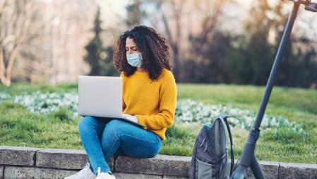 Woman wearing a face mask working on a laptop outdoors in a park