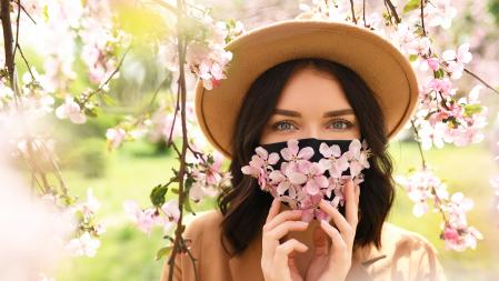 Woman wearing face mask decorated with flowers. Stylish handmade cotton mask. Spring blossom garden