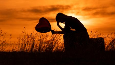 Silhouette of a sad woman sitting on suitcase with heart shaped balloon  at the sunset.