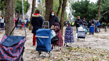 Gente con carros de la compra esperando su turno el el Parque de Aluche (Madrid) para el reparto de comida y otros materiales