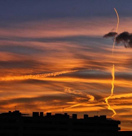 Puesta de sol en Barcelona con estelas de condensación horizontales y verticales.