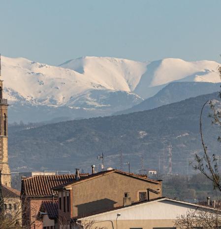 El campanario de Santa Maria de Manlleu y la ermita de Sant Jaume lucen con el Pirineo blanco de fondo.