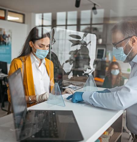 Bank teller discussing paperwork with customer at bank counter wearing protective gloves and face mask. Office with acrylic glass partition on desk. Acrylic glass wall - protection against coughs and spitting, protection against viruses.
