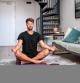 Handsome young man meditating in the living room